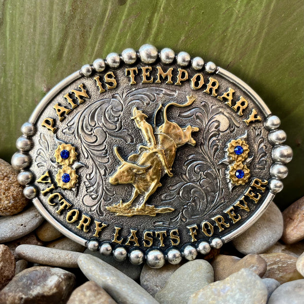 Montana Silversmiths Attitude Buckle in silver, engraved with a motivational saying, adorned with gold bull rider and floral accents with blue stone centers - A829. Available at Blair's Western Wear, Marble Falls, TX.